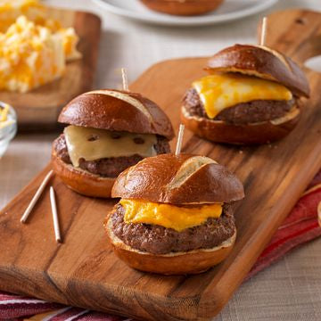 Three mini cheeseburger sliders on a wooden board with a side of cheese.
