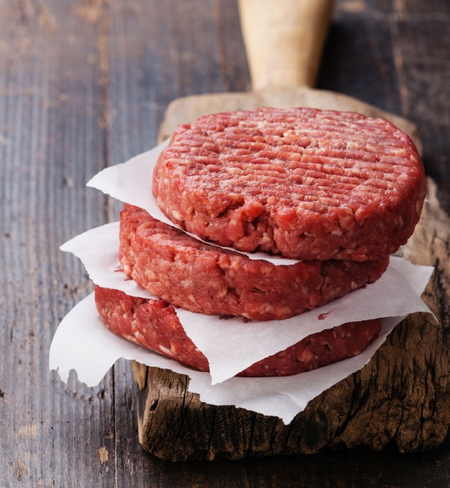 Two raw 1/2lb burger patties on a wooden surface, separated by a piece of parchment paper.