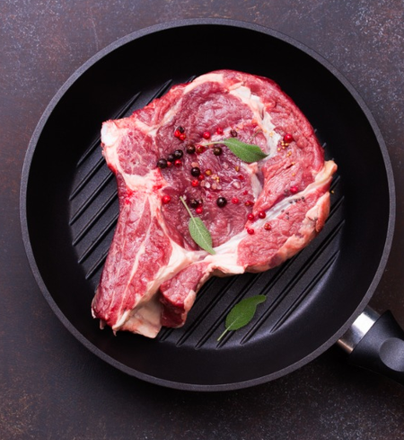 A ribeye steak with seasoning and herbs on a grill pan.