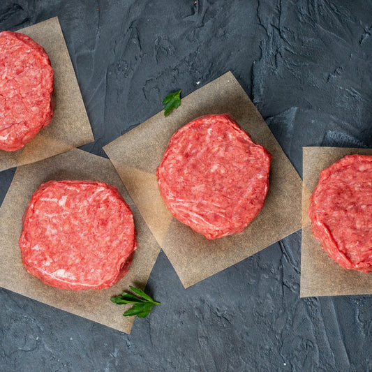 Raw hamburger patties on brown paper with a dark textured background