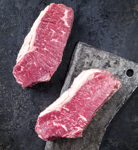 Two raw sirloin steaks on a metal cutting board, with a dark background.